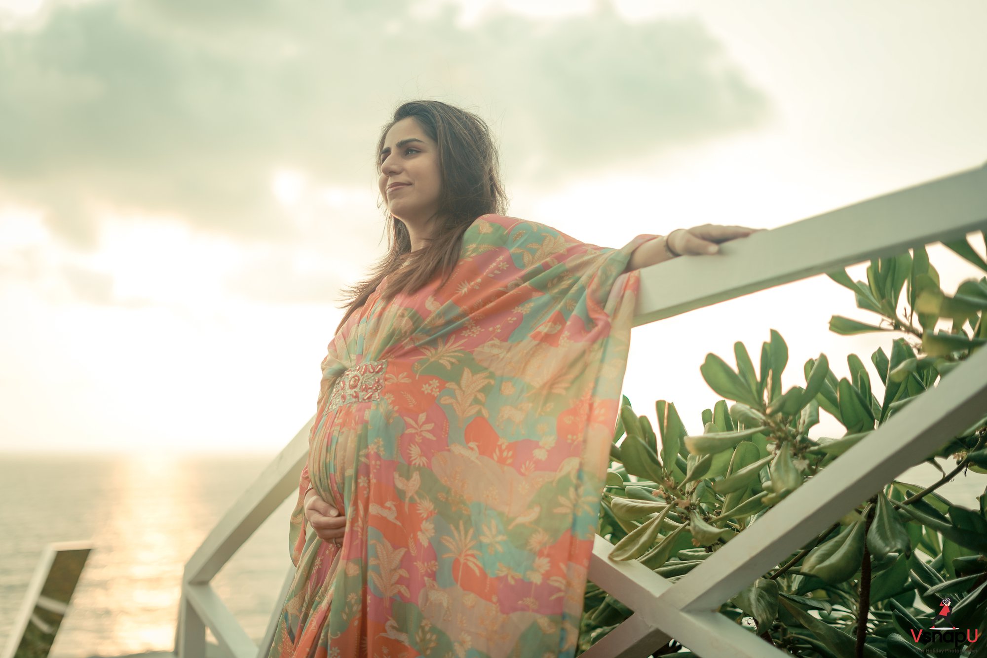 A beautiful pregnant lady touching her belly, bathed in the warmth of a sunset beachscape.